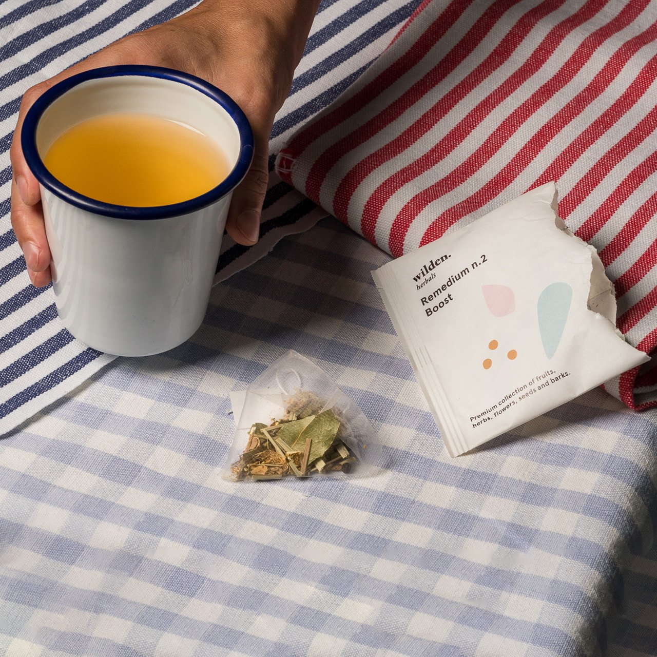 Simple cup of herbal organic infusion held by a hand with line-pattern fabrics